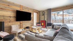 A living room with a sofa, a television, a fireplace, and a view of a snowy landscape. - Apartment 'Chalet La Turra' with Mountain View, Wi-Fi and Air Conditioning (Lanslebourg Mont Cenis)