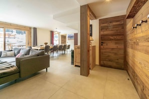 A modern living room with a sofa, dining table, and chairs. There is a wooden wall panel and a door with a handle.