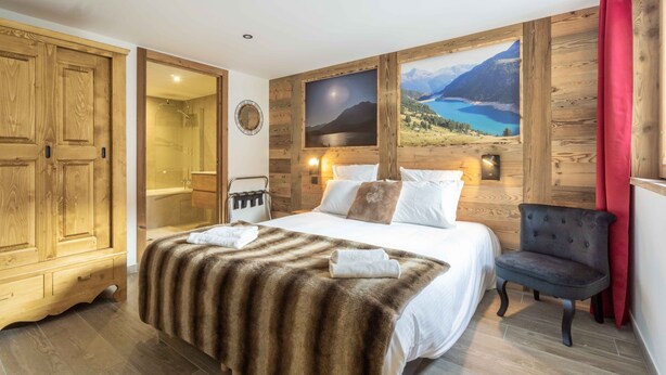 A bedroom with a large bed, wooden wardrobe, and a view of a lake through a window. - Apartment 'Chalet La Turra' with Mountain View, Wi-Fi and Air Conditioning (Lanslebourg Mont Cenis)