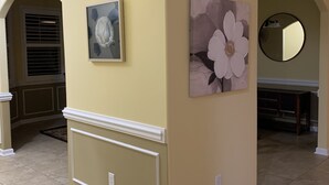 A hallway with cream walls, a large floral painting, and a round mirror.