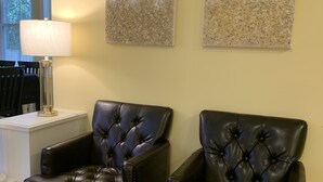 Two black leather armchairs with tufted backs, a white side table, and two abstract wall art pieces.