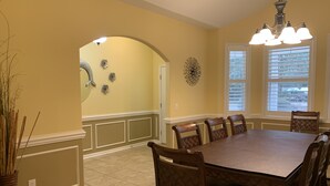 A dining room with a large wooden table, six chairs, a chandelier, and decorative wall art.