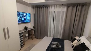 Quarto moderno com cama, televisão, escrivaninha e cortinas.