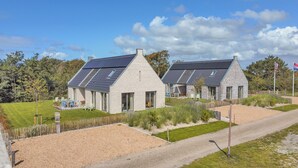 A modern house with a sloped roof, large windows, and a well-maintained garden. - Optoog XL (Callantsoog)
