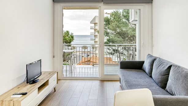 Una sala de estar moderna con televisión, sofá y balcón con vistas al mar.