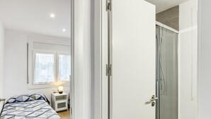 Un dormitorio con cama, mesita de noche, ventana con cortinas y zona de ducha.