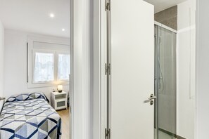 A bedroom with a bed, a nightstand, a window with curtains, and a shower area.