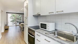 Una cocina moderna con armarios blancos, microondas integrado, pileta de acero inoxidable y puerta corrediza de vidrio que da a un balcón.
