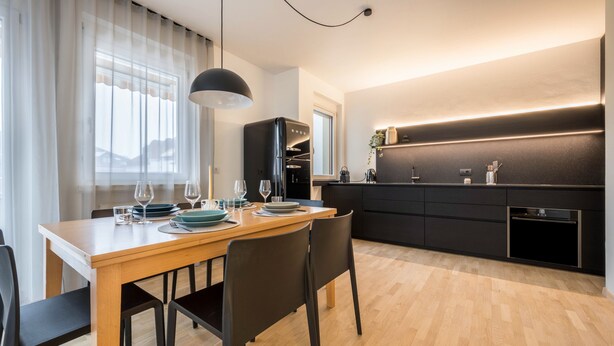 A modern kitchen with a dining table set for four, a black refrigerator, and a built-in oven. - Apartment "Avia Living" with Mountain View, Balconies & Wi-Fi (Brunico)