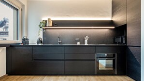 A modern kitchen with a dark countertop, built-in appliances, and a wooden floor. - Apartment "Avia Living" with Mountain View, Balconies & Wi-Fi (Brunico)