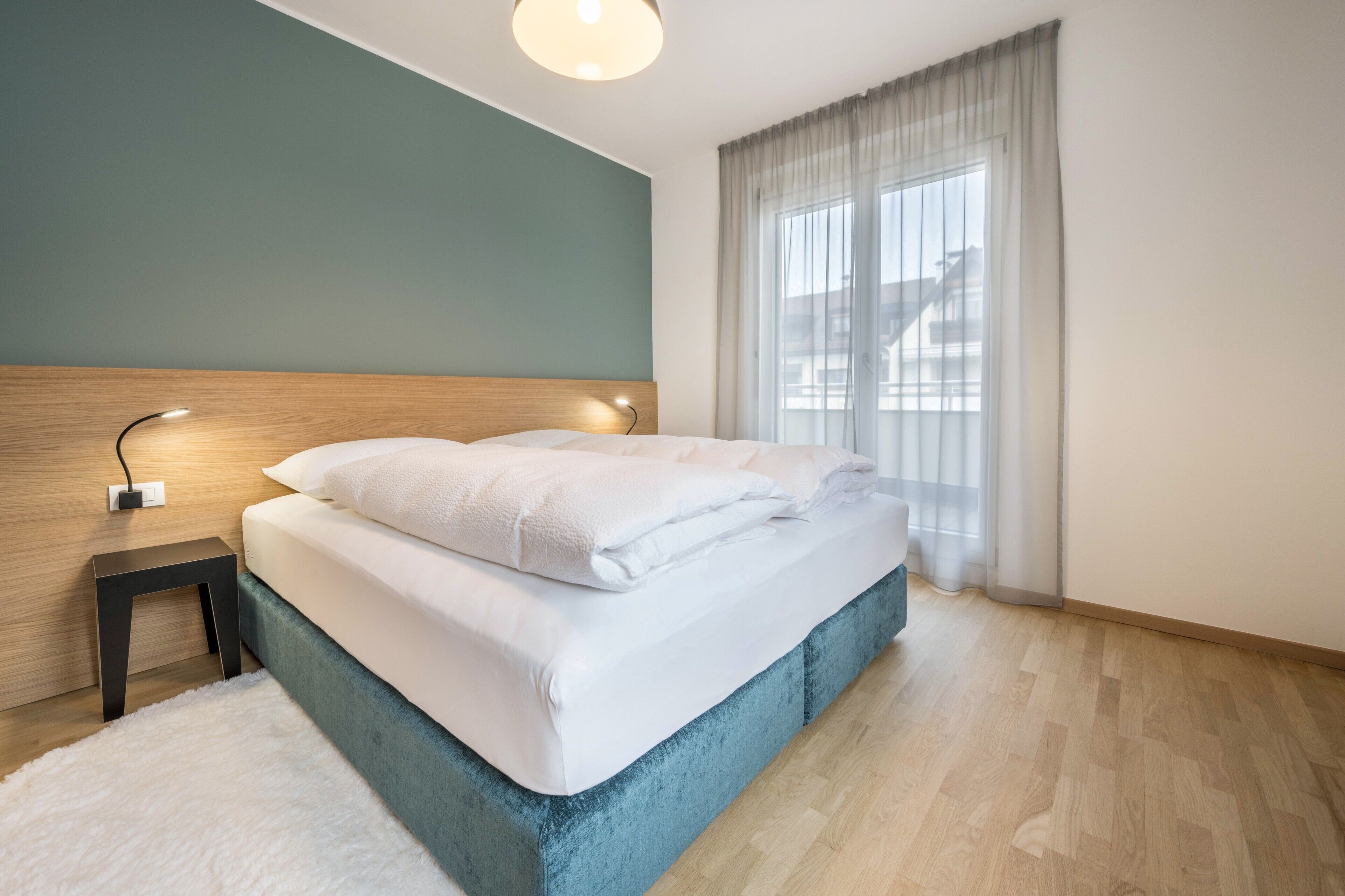 A modern hotel room with a bed, bedside table, and a window with curtains.