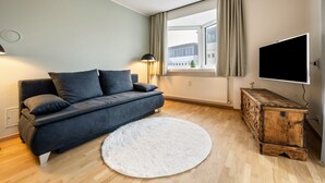 A modern living room with a sofa, a round rug, a wooden cabinet, a TV, and a window with curtains. - Apartment "Avia Living" with Mountain View, Balconies & Wi-Fi (Brunico)
