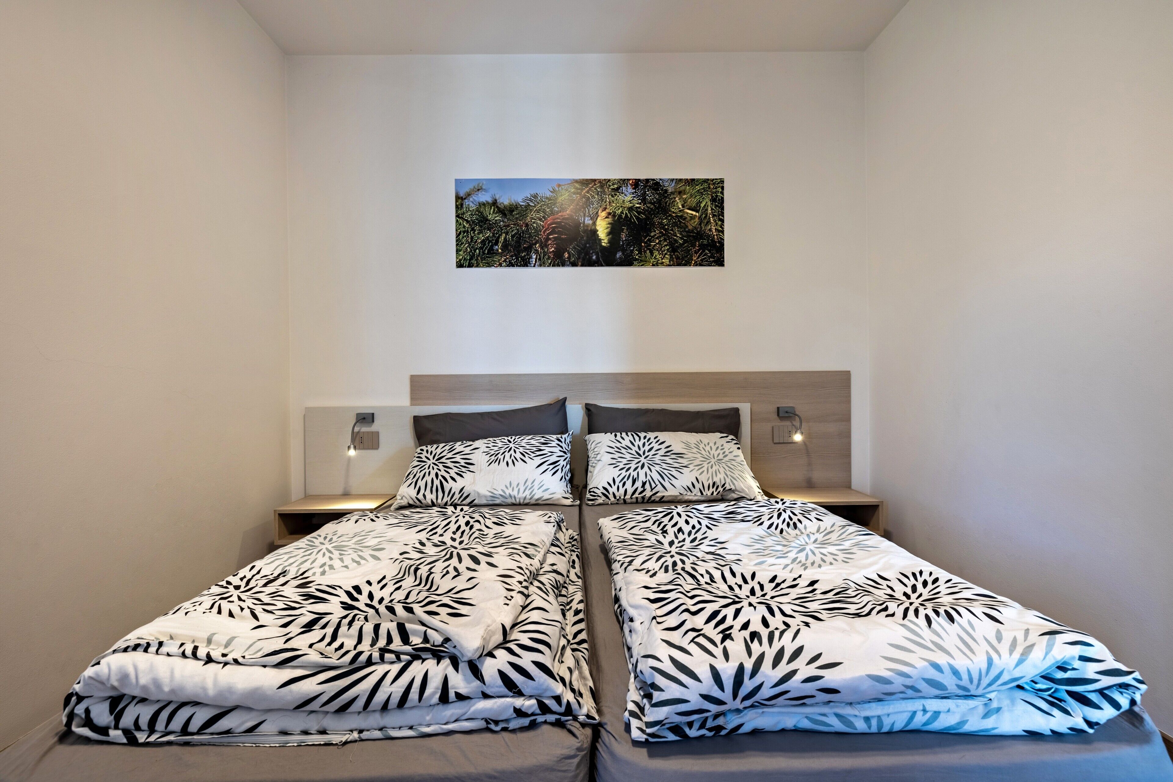 Un lit double avec une couvre-lit à motifs de feuilles, une table de chevet avec une lampe et un tableau encadré au mur.