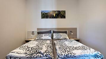 Un lit double avec une couvre-lit à motifs de feuilles, une table de chevet avec une lampe et un tableau encadré au mur.