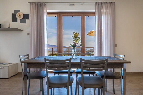 Un espace repas comprenant une table, des chaises, un vase avec des fleurs et une vue sur l’extérieur.