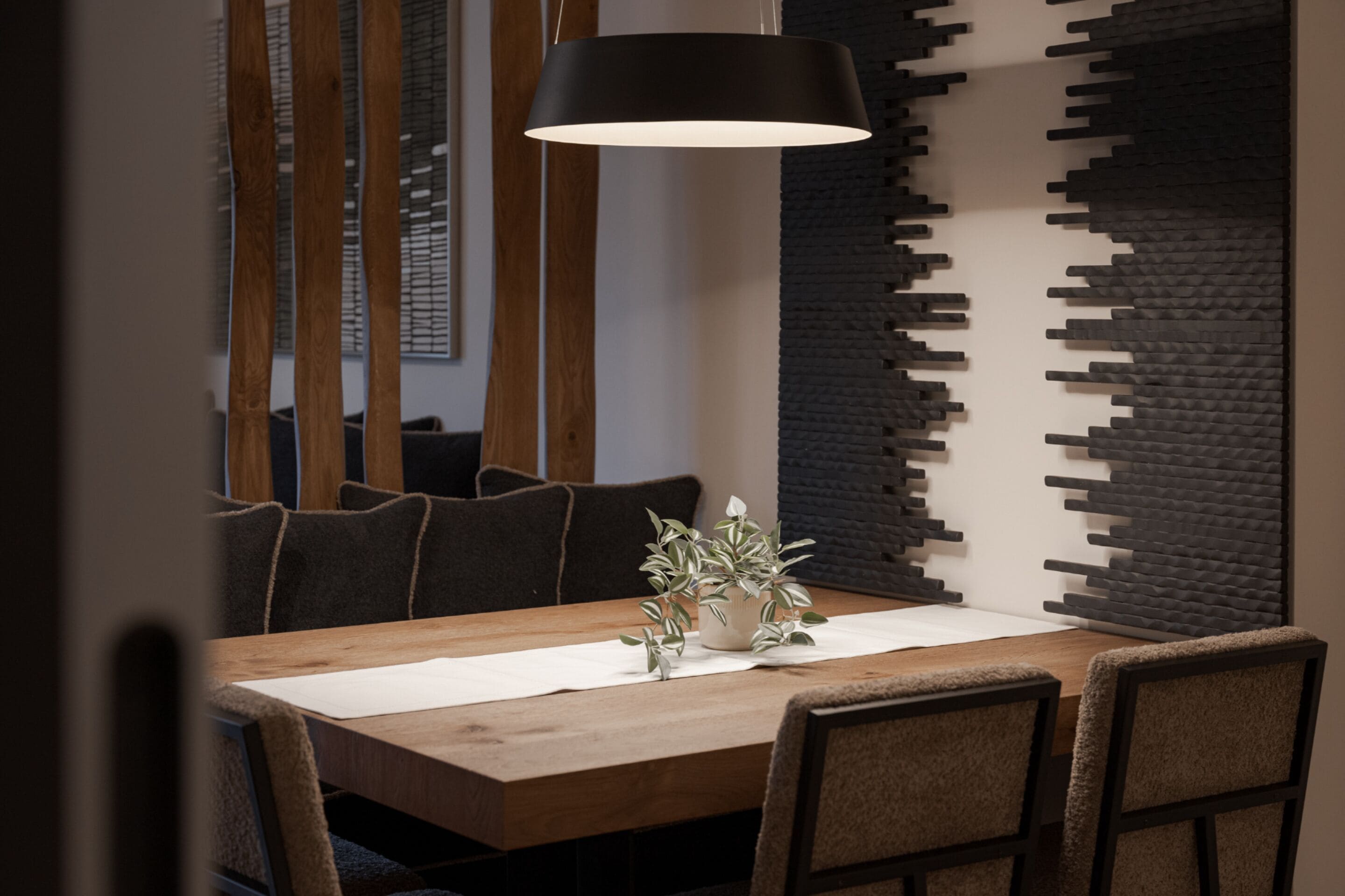 Un comedor con una mesa de madera, sillas, una lámpara colgante y una pared con textura.