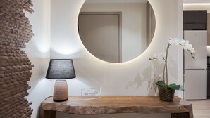 Una mesa de madera con una lámpara y un letrero, un espejo redondo y una orquídea en maceta.