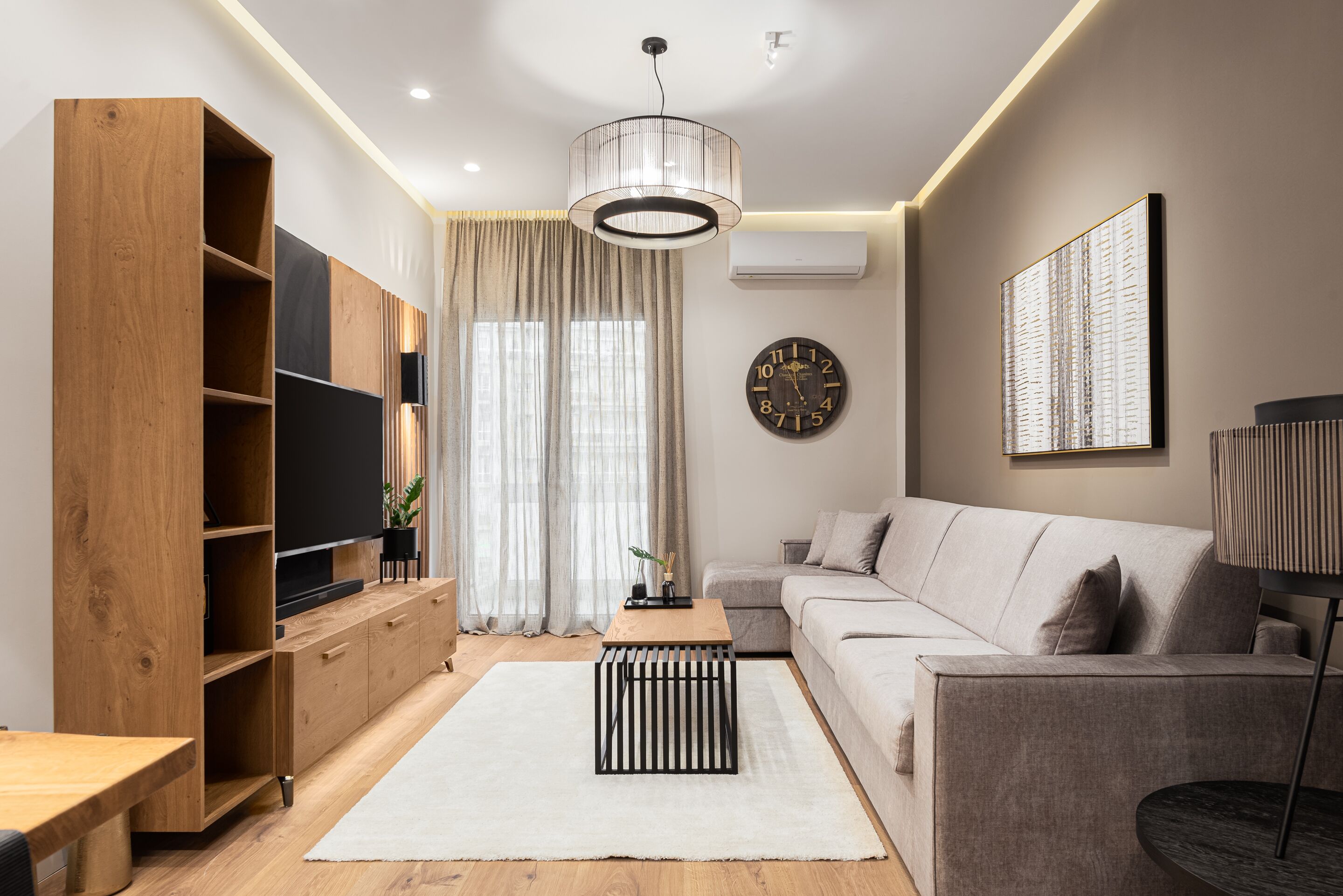 A modern living room with a wooden entertainment unit, a sofa, a coffee table, and a large clock on the wall.