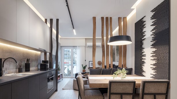 Una cocina moderna con una isla central, un comedor con mesa y sillas de madera, e instalación artística original en la pared.