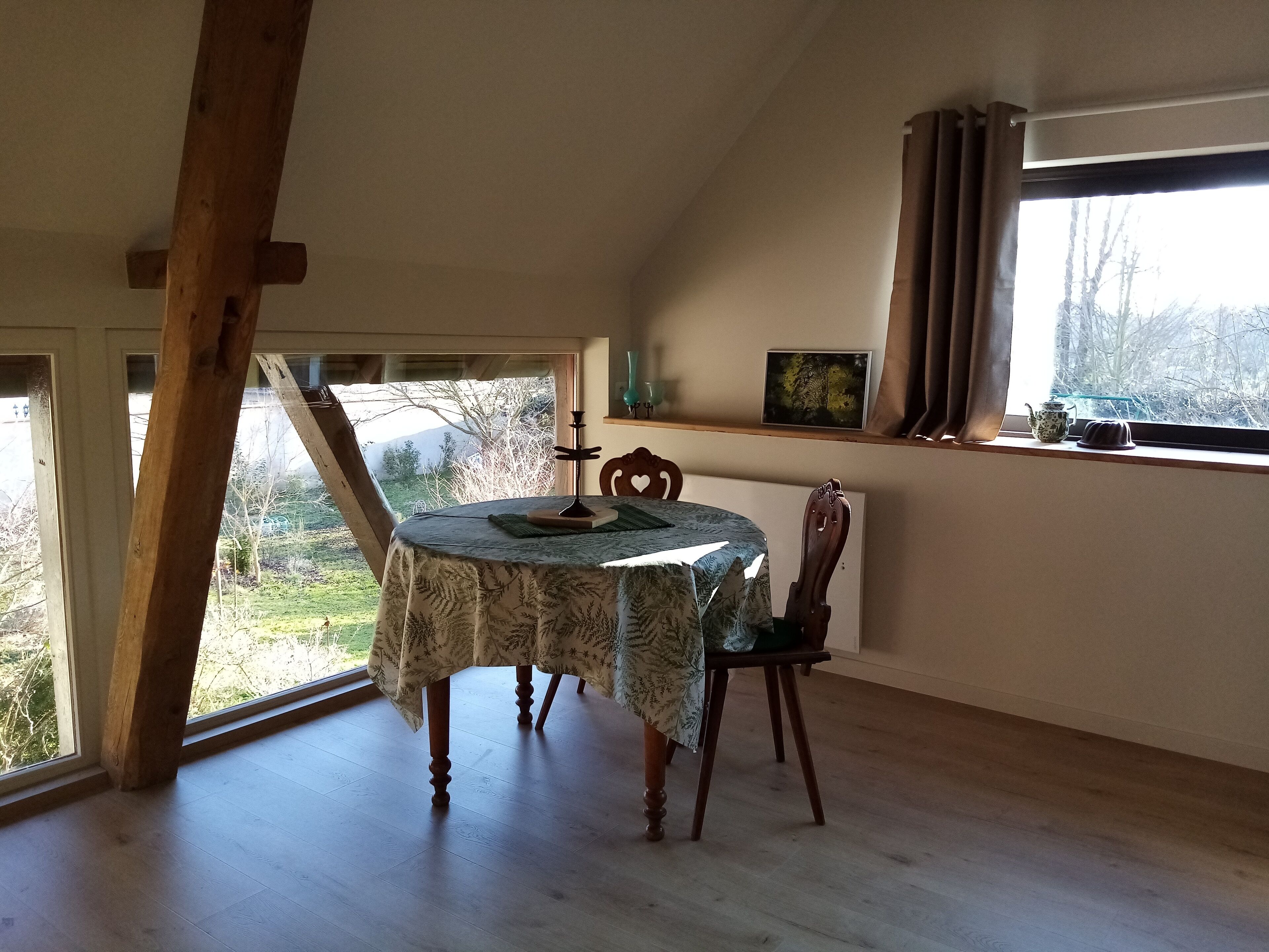 Un comedor con mesa y sillas, una ventana que da a vistas de árboles, y una viga de techo de madera.
