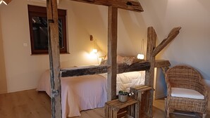Un dormitori rústic amb bigues de fusta a la vista, un llit individual, una cadira de vimet i una taula de fusta petita amb una planta.