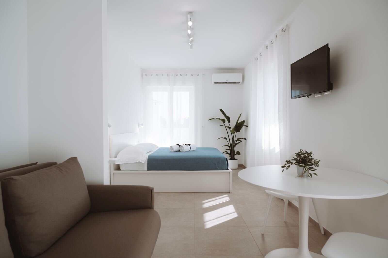 A minimalist bedroom with a bed, a TV, a small table, and a sofa.