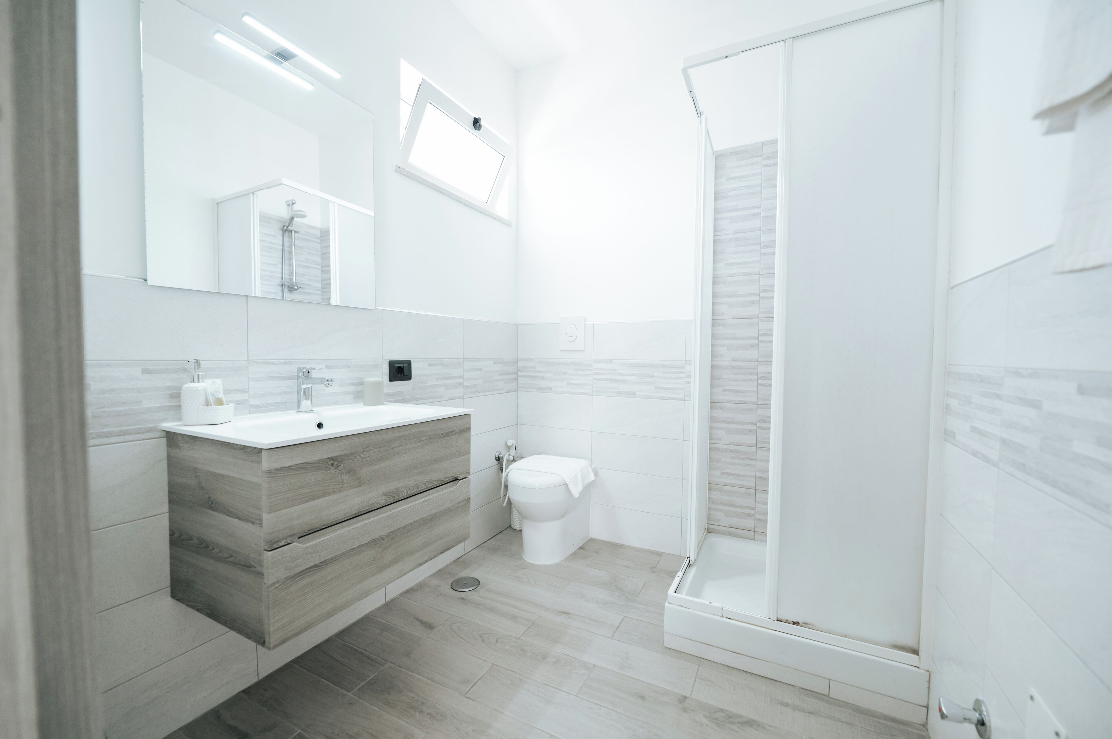 Une salle de bain moderne avec un grand miroir, un meuble-lavabo en bois, des toilettes et une douche à parois de verre.