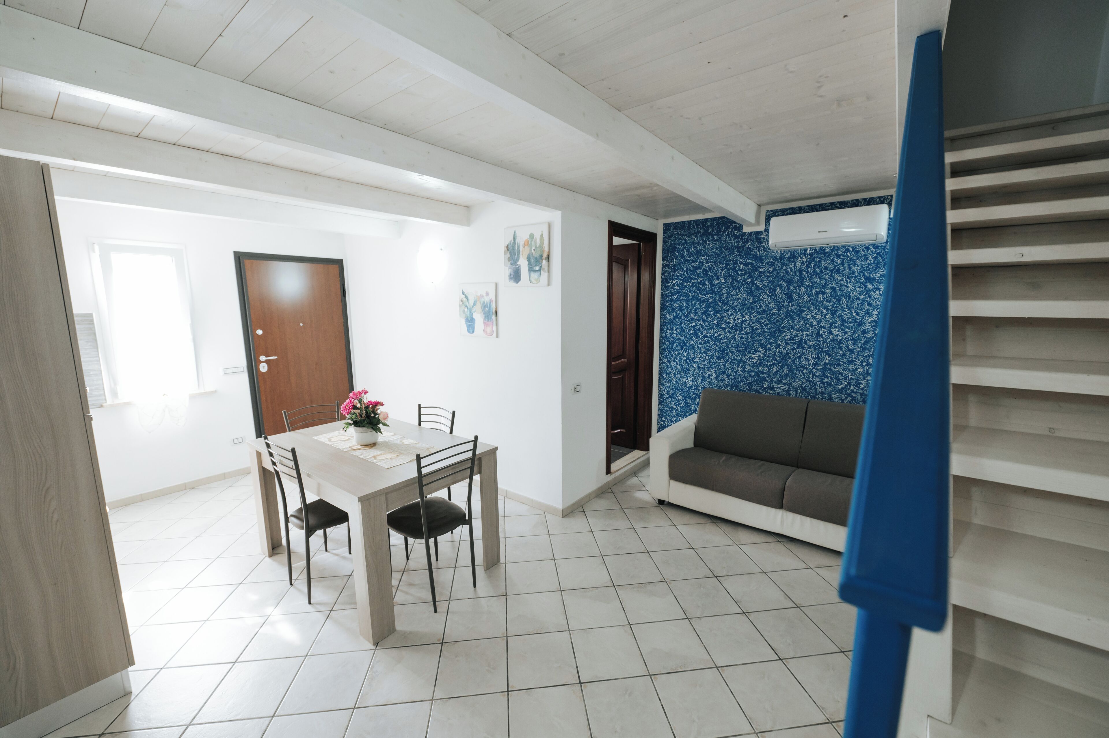 A spacious living area with a dining table, chairs, a sofa, and a staircase.