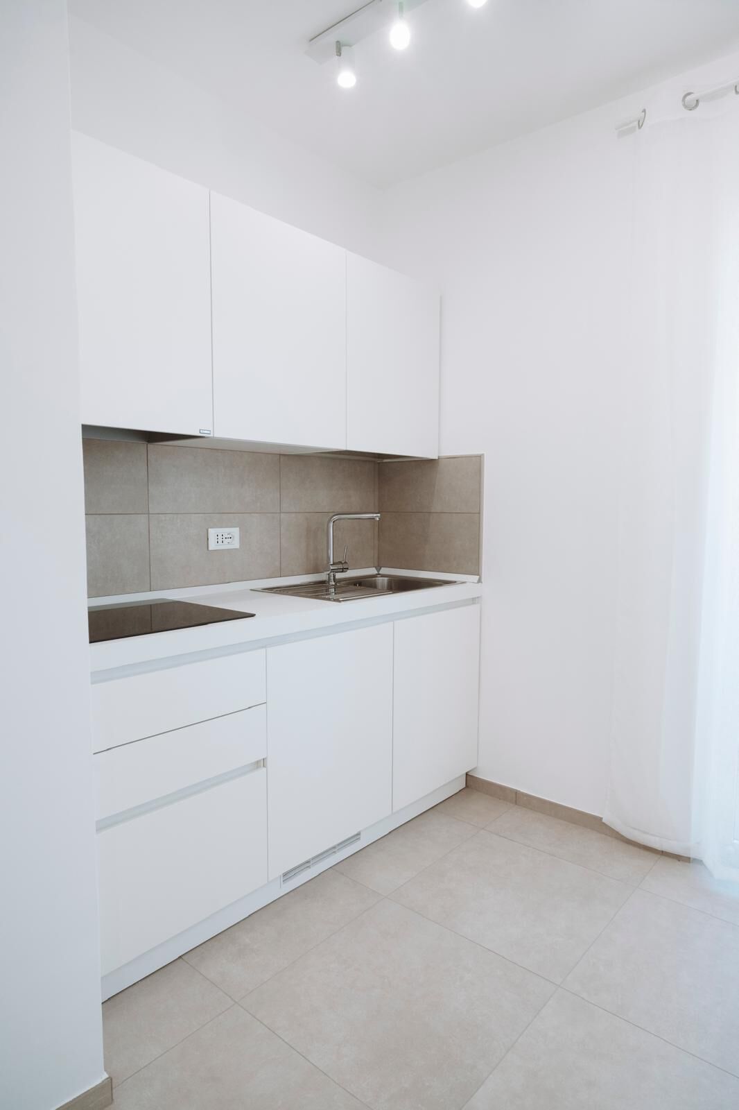 Una cocina moderna con gabinetes blancos, un lavamanos de acero inoxidable y un salpicadero de azulejos.