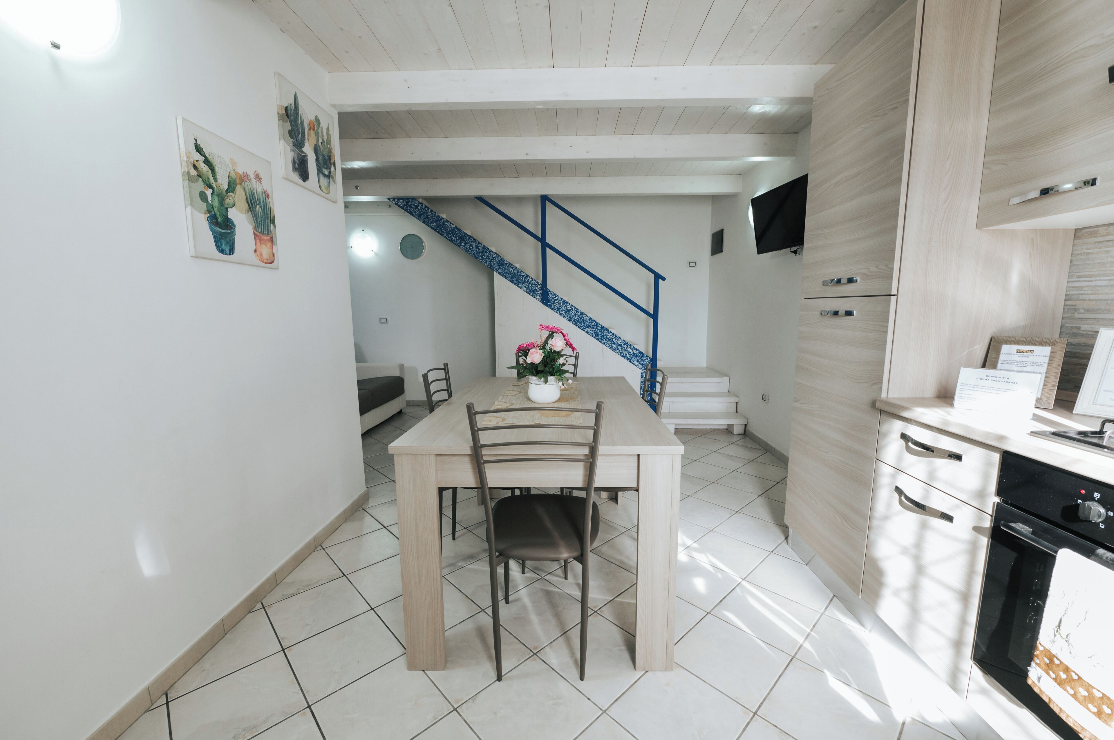 Una cocina moderna con comedor, una escalera y un televisor de pantalla plana en la pared.