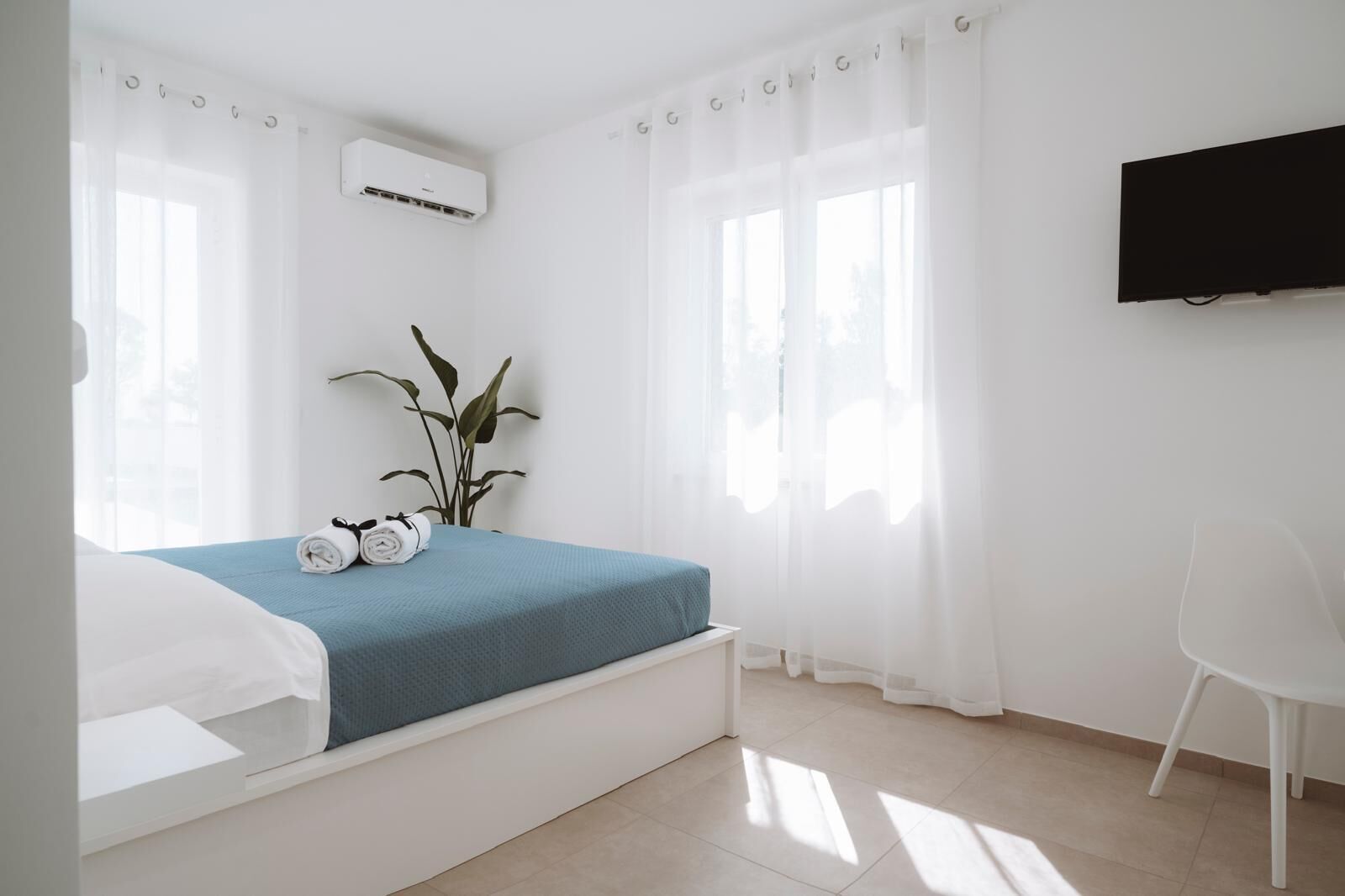 A modern hotel room with a bed, a TV, a plant, and a chair.