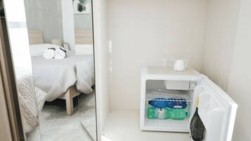 Una camera d'albergo con un letto, un bagno piccolo e un frigorifero con acqua in bottiglia e una bottiglia di champagne.