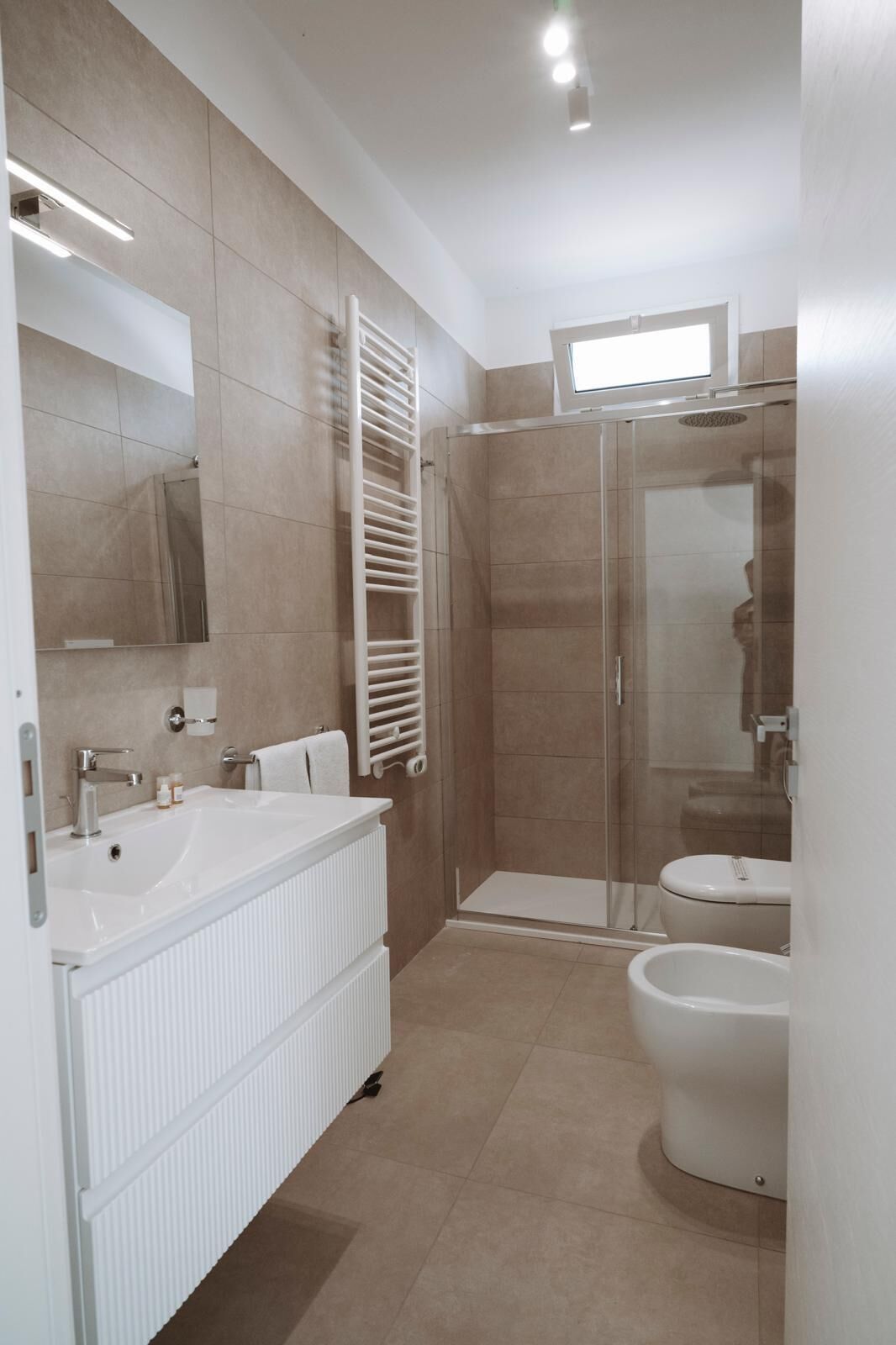 Un baño moderno con un lavamanos grande de color blanco, cabina de ducha de vidrio y un inodoro.
