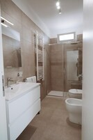 Un baño moderno con un lavamanos grande de color blanco, cabina de ducha de vidrio y un inodoro.