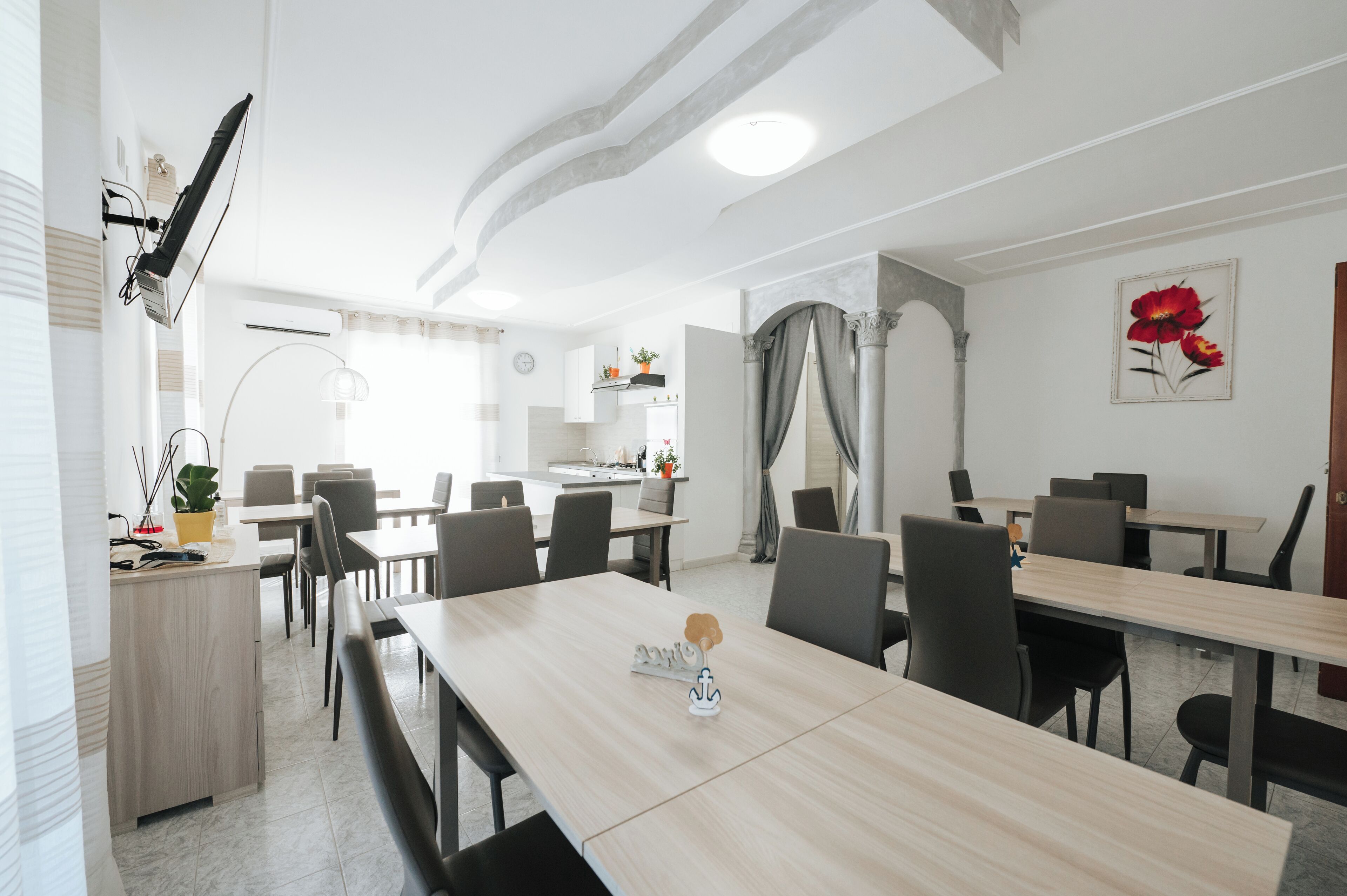 A modern dining area with multiple tables and chairs, a kitchen in the background, and a decorative plant on the counter.