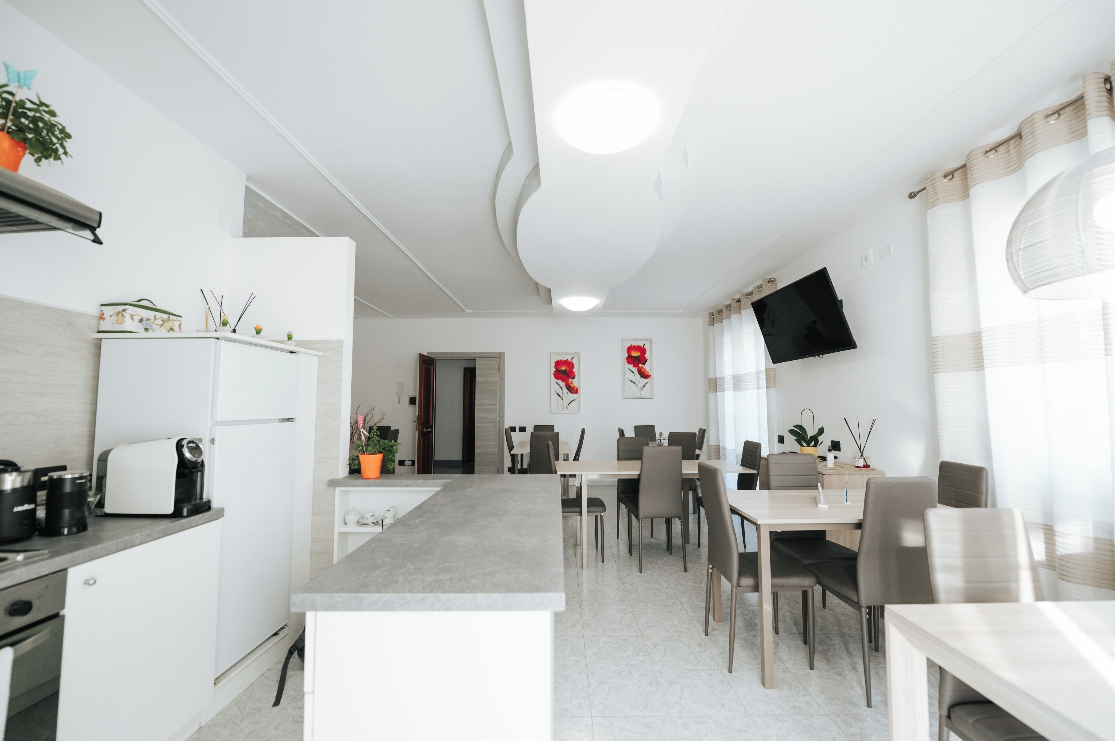 Une cuisine moderne avec un coin repas, des meubles blancs, un téléviseur à écran plat et une grande fenêtre avec des rideaux.