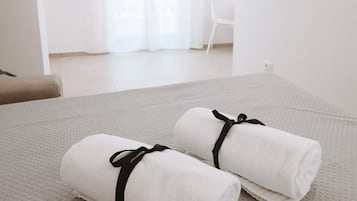Relax in a serene space with a neatly made bed, a comfortable chair, and a large window with sheer curtains.