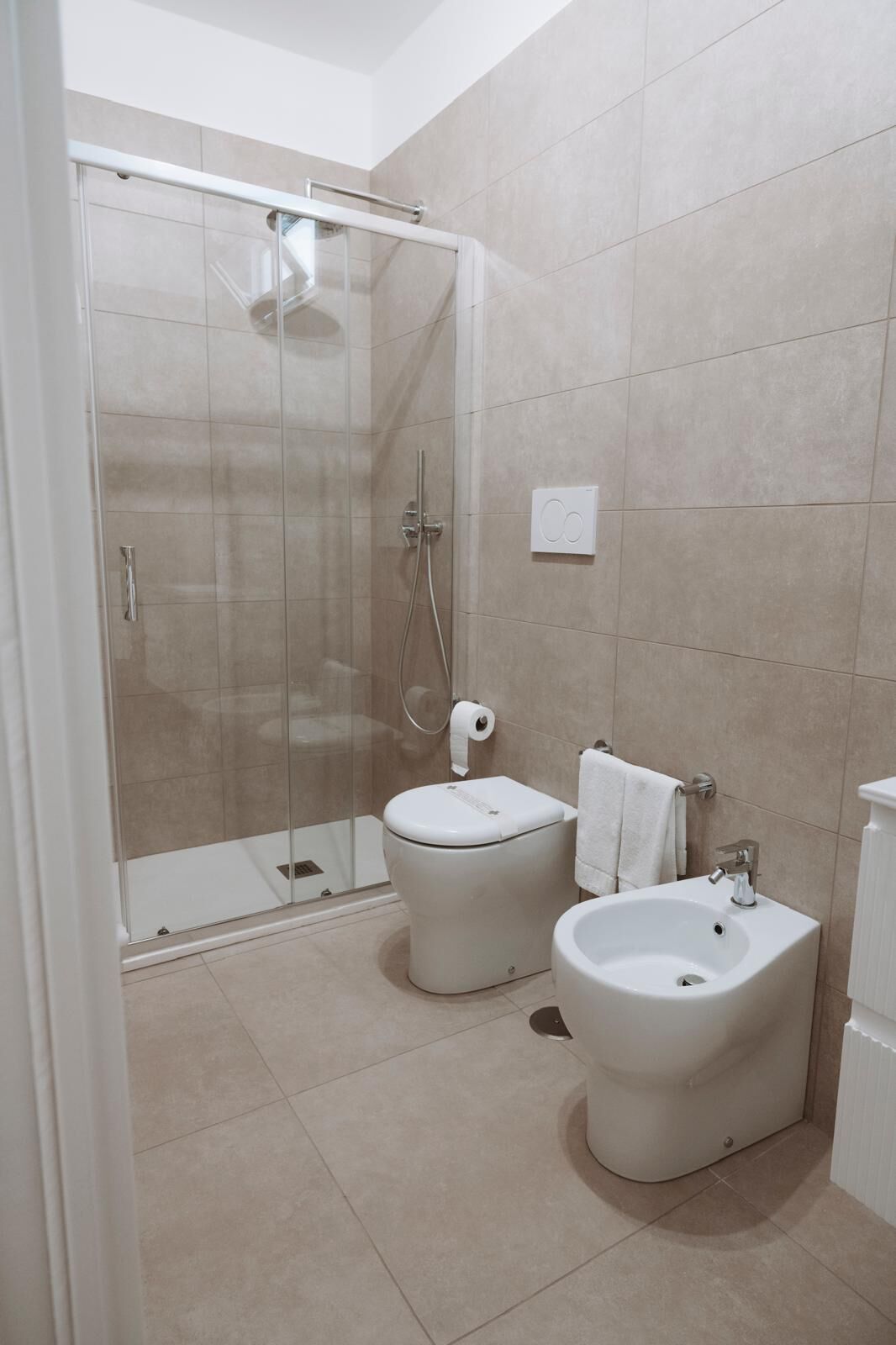 A modern bathroom with a glass-enclosed shower, a toilet, a bidet, and a sink.