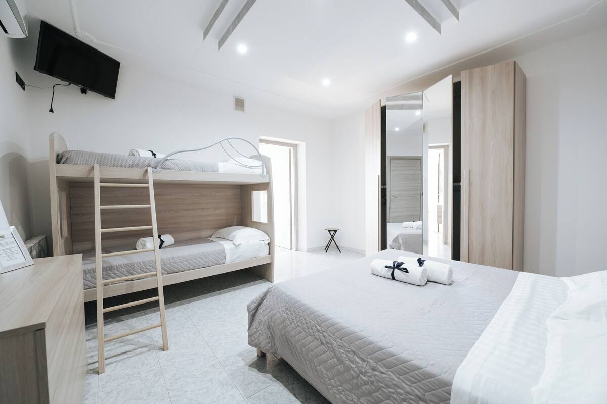 Quarto de hotel moderno com beliche, escrivaninha, TV de tela plana na parede e um espelho grande.