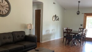 A living room with a dark brown sofa, a wooden coffee table, and a patterned rug. There is a dining area with wooden chairs and a table, and a ceiling fan above. - Quality comfort in a convenient location (entire house) (Beaufort)