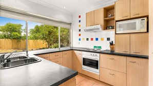 Una cocina moderna con armarios de madera, un lavamanos de acero inoxidable, horno integrado y microondas.