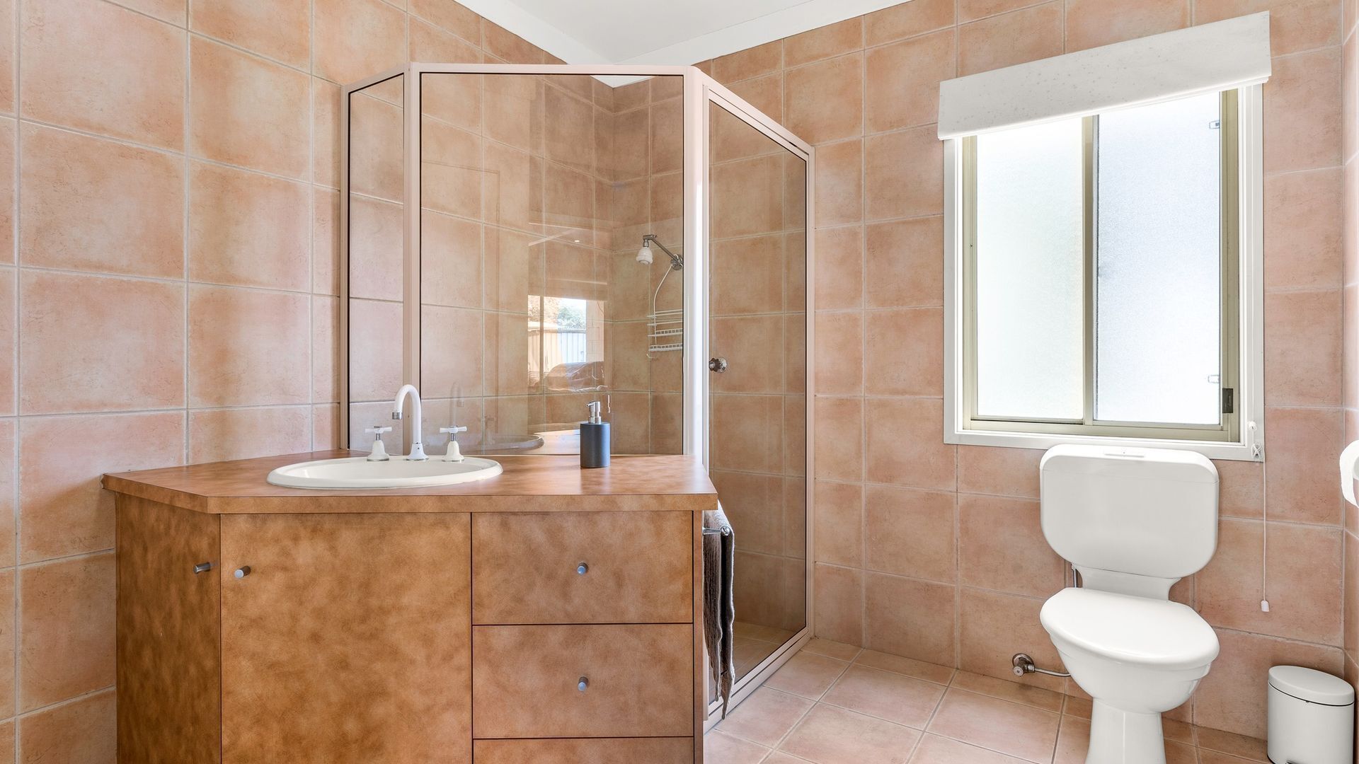 A bathroom with a sink, mirror, vanity, shower, toilet, and a window.