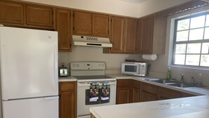 A kitchen with wooden cabinets, a white refrigerator, a stove, a microwave, and a window with a view. - Cute home, great for MCRD families (entire home) (Beaufort)