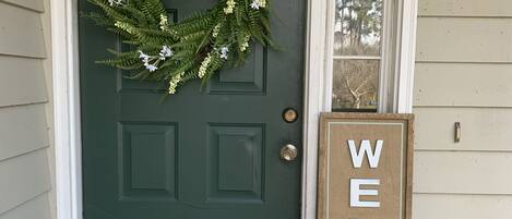 A green door with a wreath, a welcome sign, and a doormat.