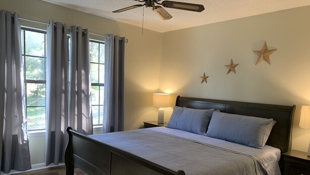 A bedroom with a wooden bed, a ceiling fan, and a window with curtains. - Cute home, great for MCRD families (entire home) (Beaufort)