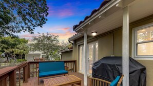 Eine überdachte Terrasse im Freien mit Holzmöbeln, einem Grill und Blick auf die Nachbarhäuser.