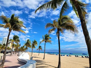 Una playa con palmeras, una estructura blanca y sombrillas azules.