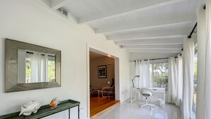 Ein modernes, helles Zimmer mit einem großen Spiegel, einem Schreibtisch mit Stuhl und Blick ins Freie durch ein Fenster.