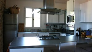 A modern kitchen with a central island, stainless steel appliances, and a large window providing natural light. - Architect's converted olive mill in historic town with garden and heated pool (Lorgues)
