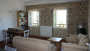 A living room with a stone wall, a sofa, a table, and a television. - Architect's converted olive mill in historic town with garden and heated pool (Lorgues)